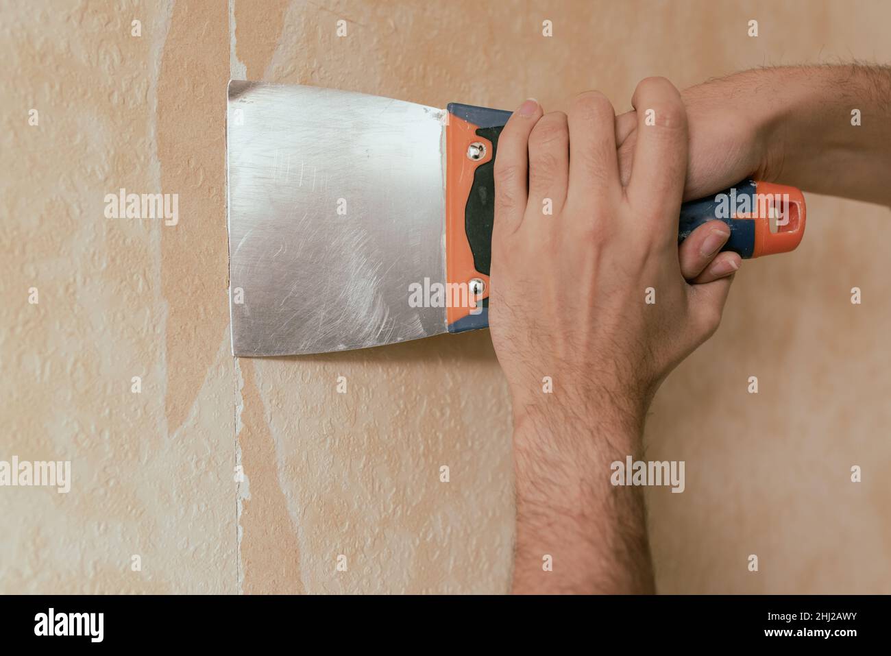Man hand tearing off old wallpaper with scraper from wall. Stock Photo