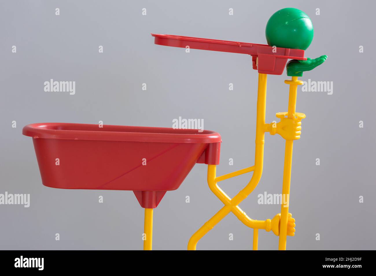 A close up of the green bowling ball resting above the Green helping Hand supported by the yellow plumbing., which connects to the red bath. Stock Photo