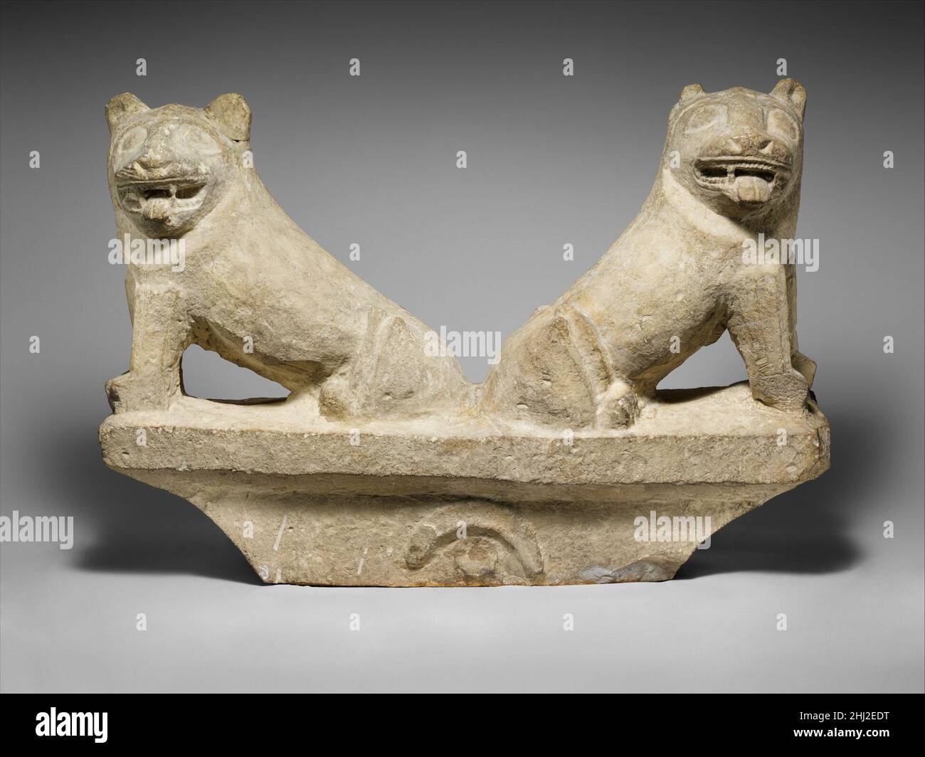 Limestone finial of a funerary stele with two seated lions ca. 550–526 B.C. Cypriot Two lions sit back to back on a cavetto finial decorated with a disk and a crescent, the points of which turn downward. The lions’ heads are turned toward the viewer, their mouths open and tongues extended.. Limestone finial of a funerary stele with two seated lions  242415 Stock Photo