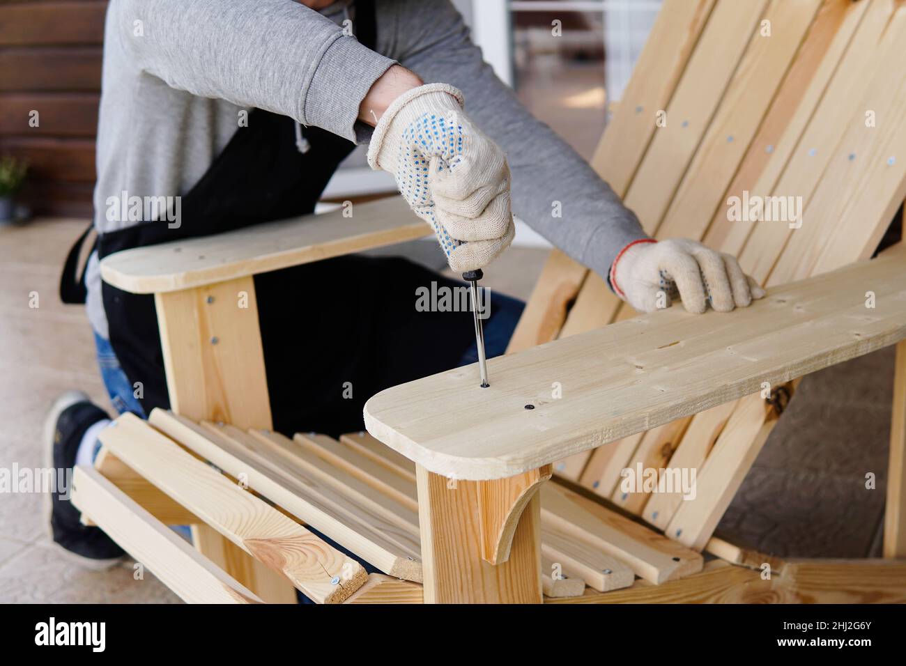 Professional carpenter assembling wooden adirondack chair with screwdriver. Manual work and do