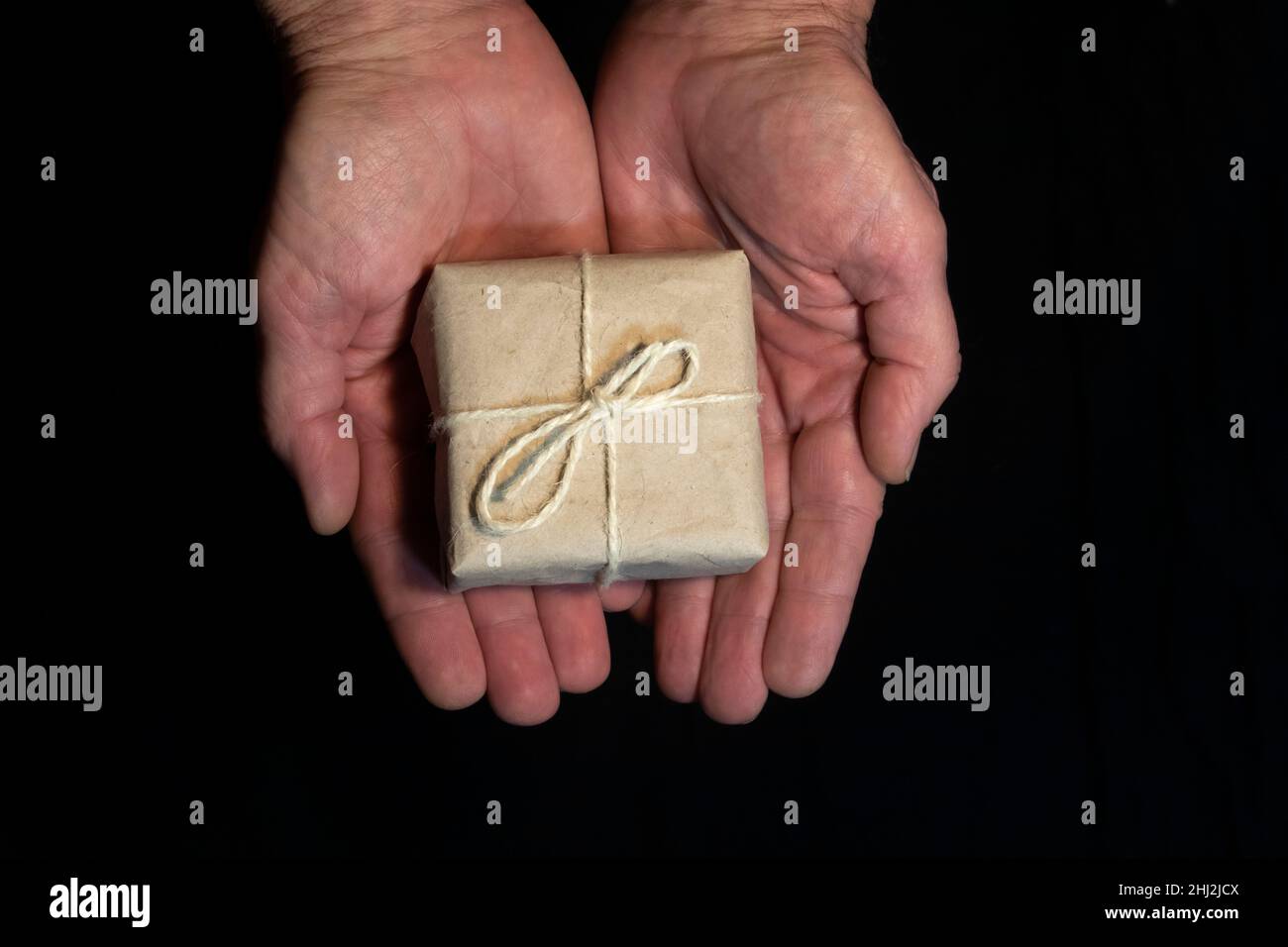 Small box with a gift in hands on a black background. Stock Photo