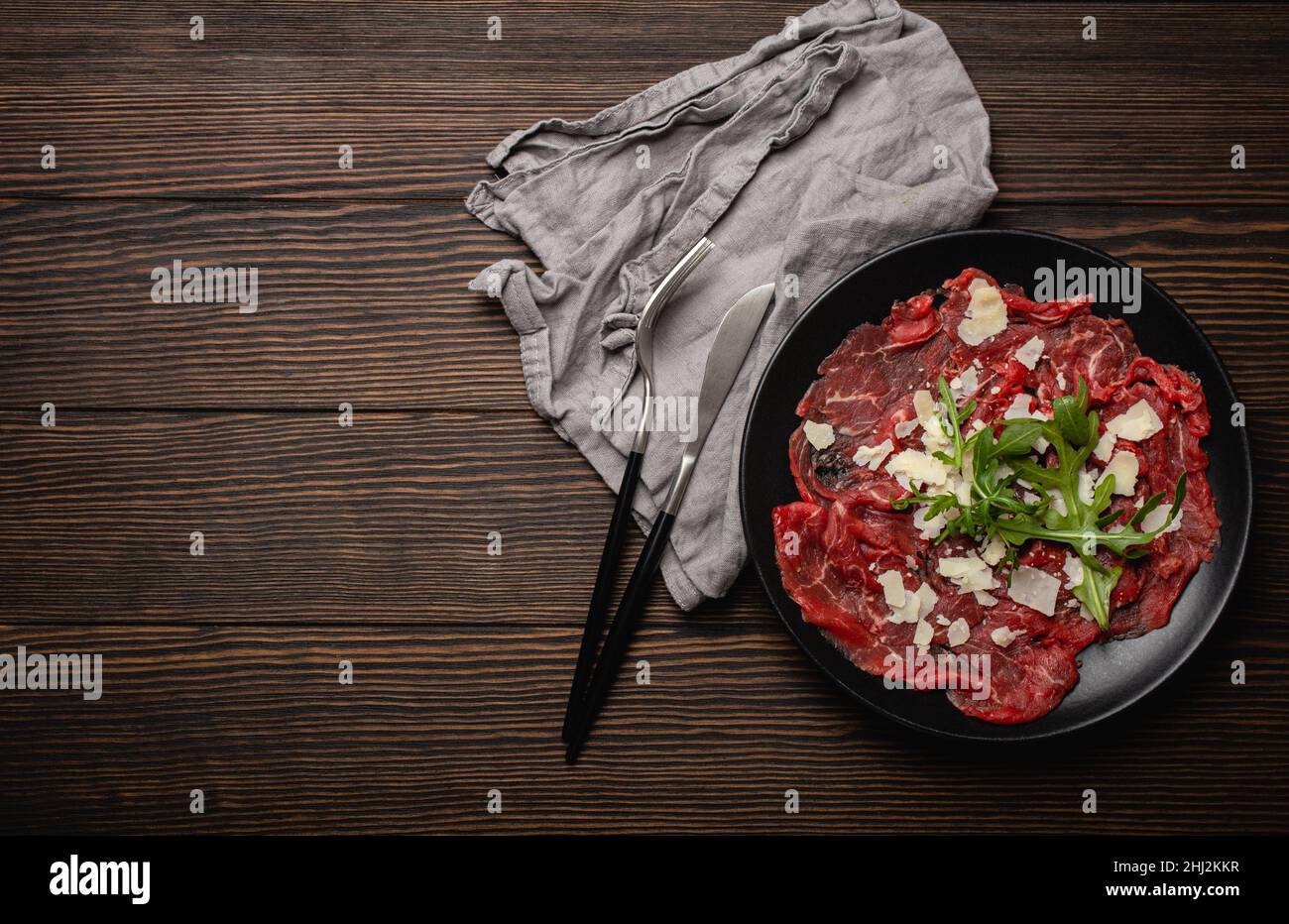 Cold meat appetizer Beef carpaccio with parmesan cheese and arugula on black plate Stock Photo