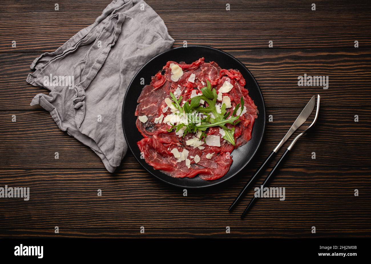 Cold meat appetizer Beef carpaccio with parmesan cheese and arugula on black plate Stock Photo