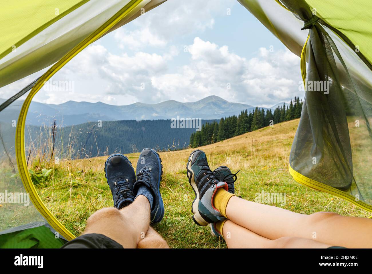 Pair of feets in hiking shoes on the background of beautiful mountain view. Couple lying inside the tent in camp and relaxing after trekking. Concept of active lifestyle, freedom and travel. Stock Photo