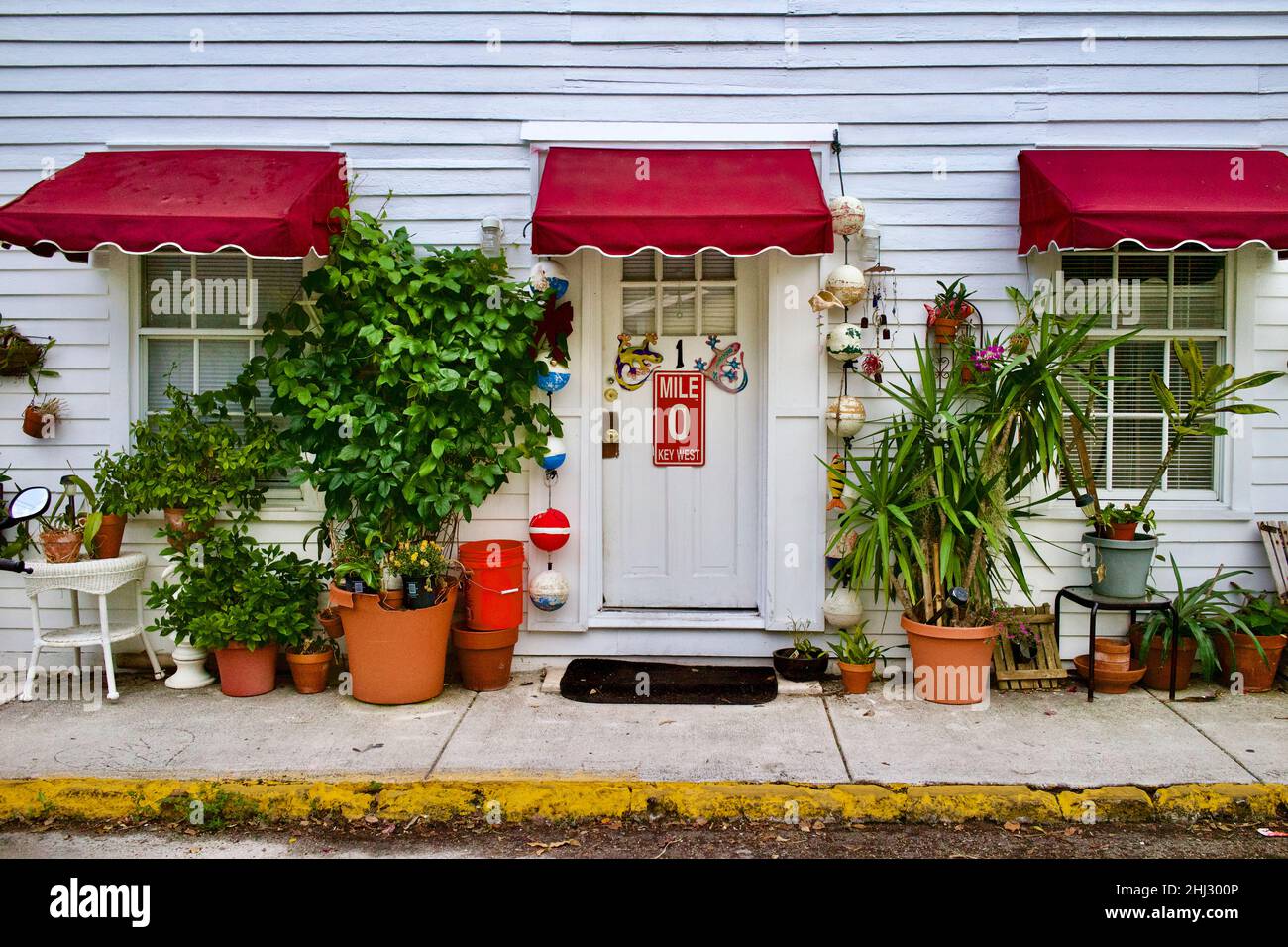Front door with Mile Marker “0” and decorative geckos in Key West, Florida, FL, USA.  Hanging fishing buoys and a red awning surround the door. Stock Photo