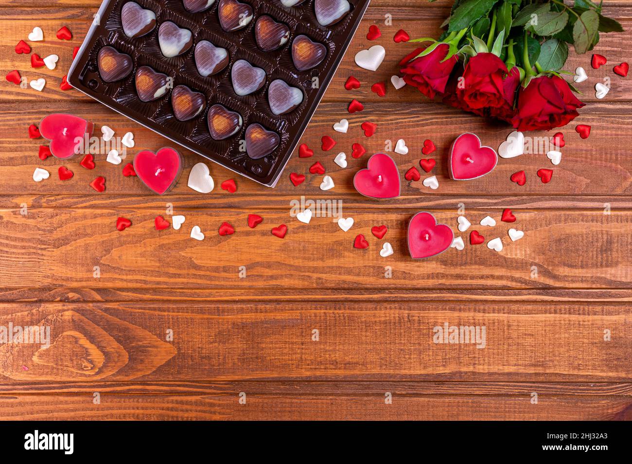 Valentines Day concept chocolate candies heart shaped and red roses with candles on wood. Love and romance concept. Stock Photo