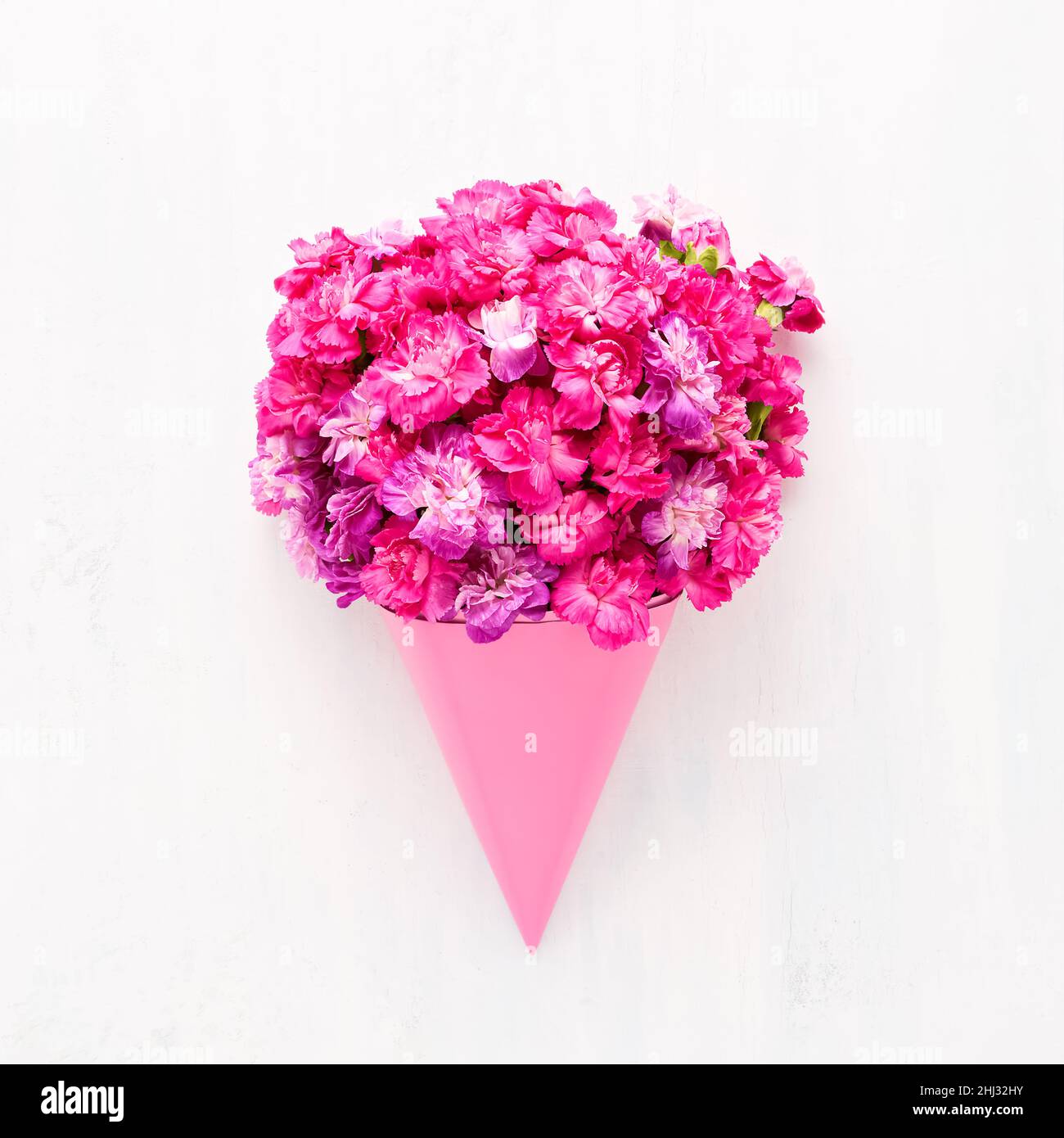 Pink carnation flowers bouquet in a pink cone on a white wooden ...