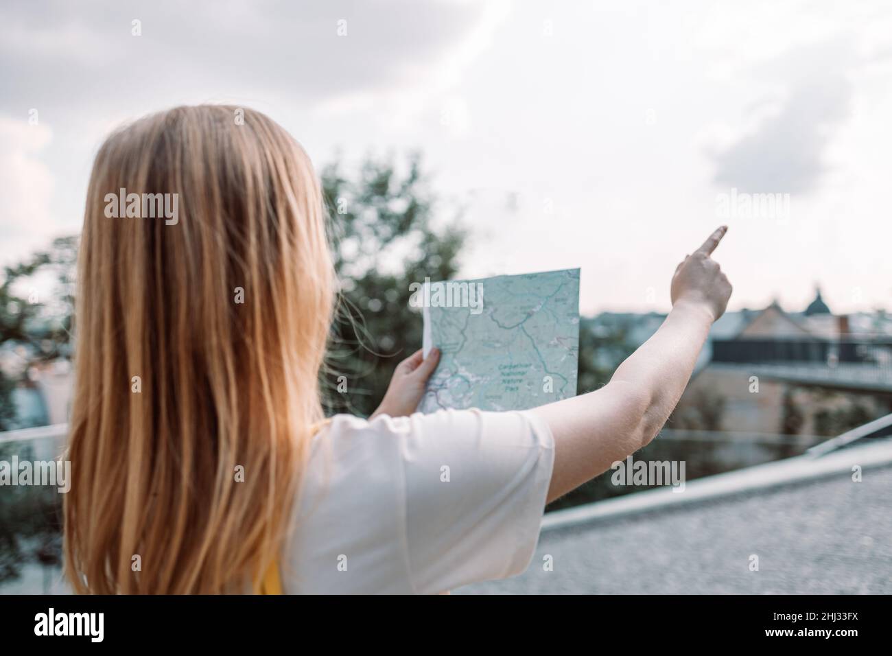 Cheerful woman searching direction on location map while traveling. Back view Stock Photo