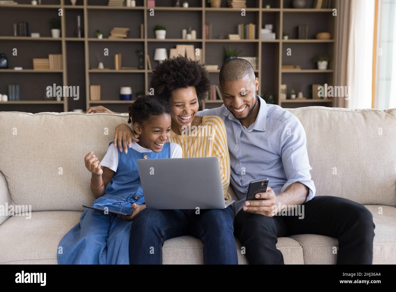 African family holding diverse devices watching on cellphone funny videos Stock Photo
