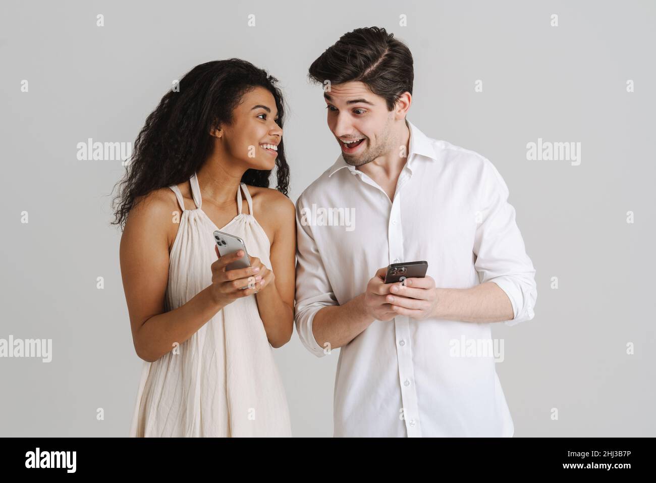 Young multiracial couple smiling while using mobile phones isolated over white background Stock Photo