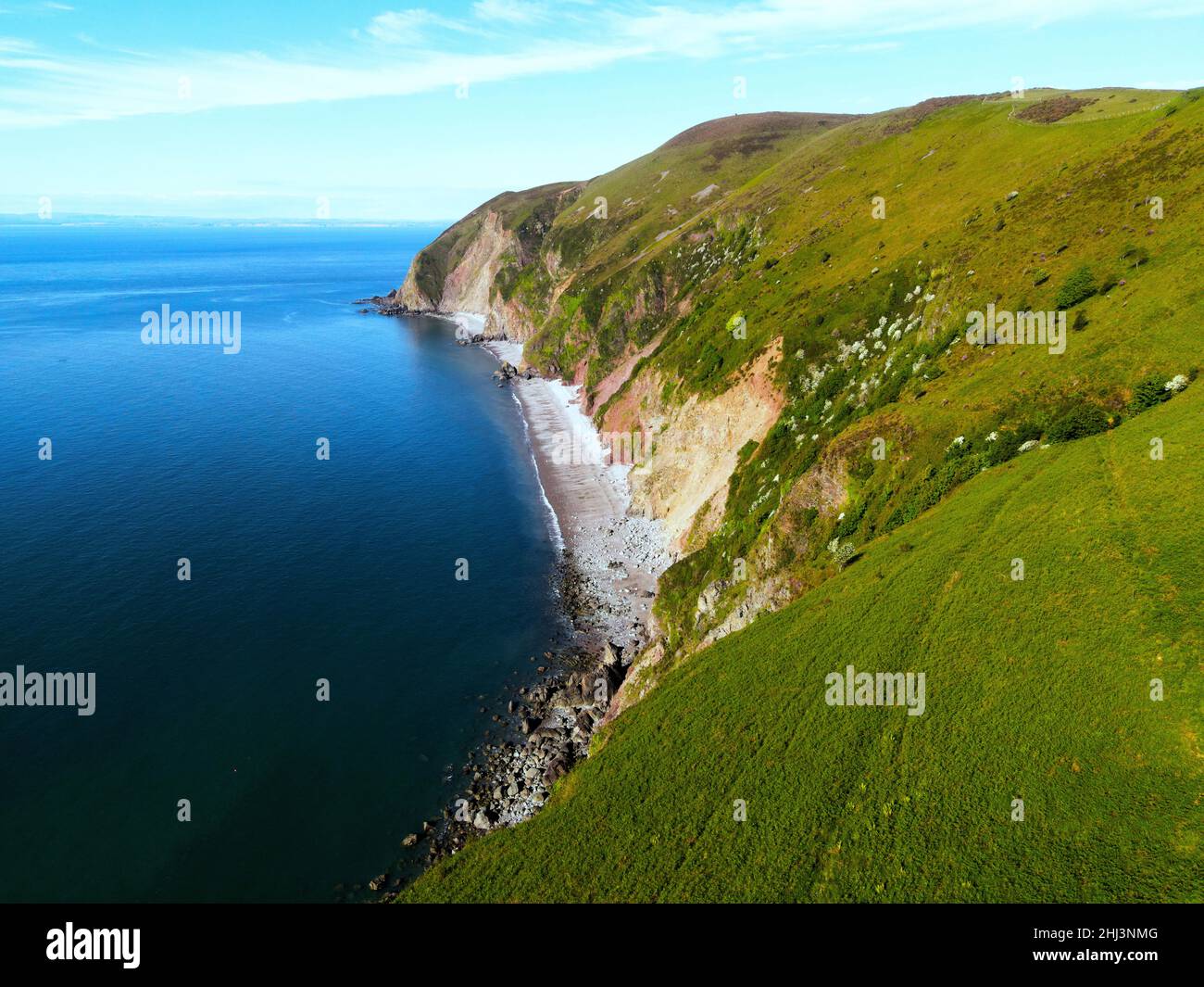 Cliff/Rock face with a stoney beach leading into a deep rich blue sea ...