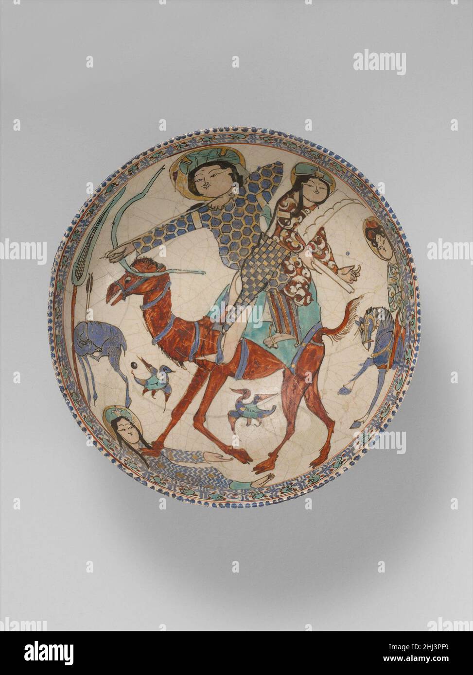 Bowl with Bahram Gur and Azada late 12th–early 13th century Bahram Gur, challenged by his concubine Azada in a series of dares to show his mastery in archery, here pins together with a single arrow the ear and hoof of a gazelle, while Azada plays the harp. The tragic epilogue of this story from the Persian epic Shahnama, in which a camel tramples Azada after she disparages the prince for his cruel feats, is portrayed at the bottom of the bowl. This popular episode was depicted on ceramics and metalware.. Bowl with Bahram Gur and Azada. late 12th–early 13th century. Stonepaste; glazed (opaque m Stock Photo