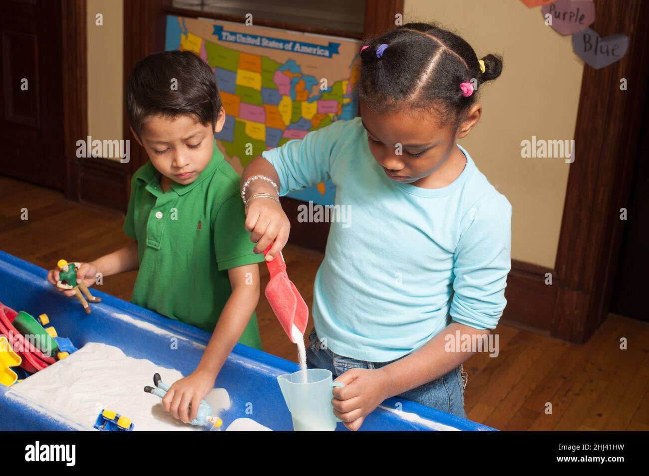 Education Preschool 4-5 year olds boy and girl playing side by side at sand table girl much taller than boy Stock Photo