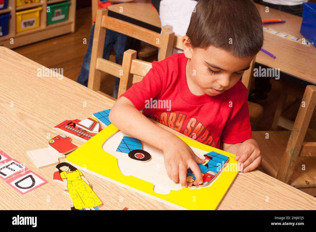 Education Preschool boy sitting at table playing with wooden firetruck puzzle Stock Photo