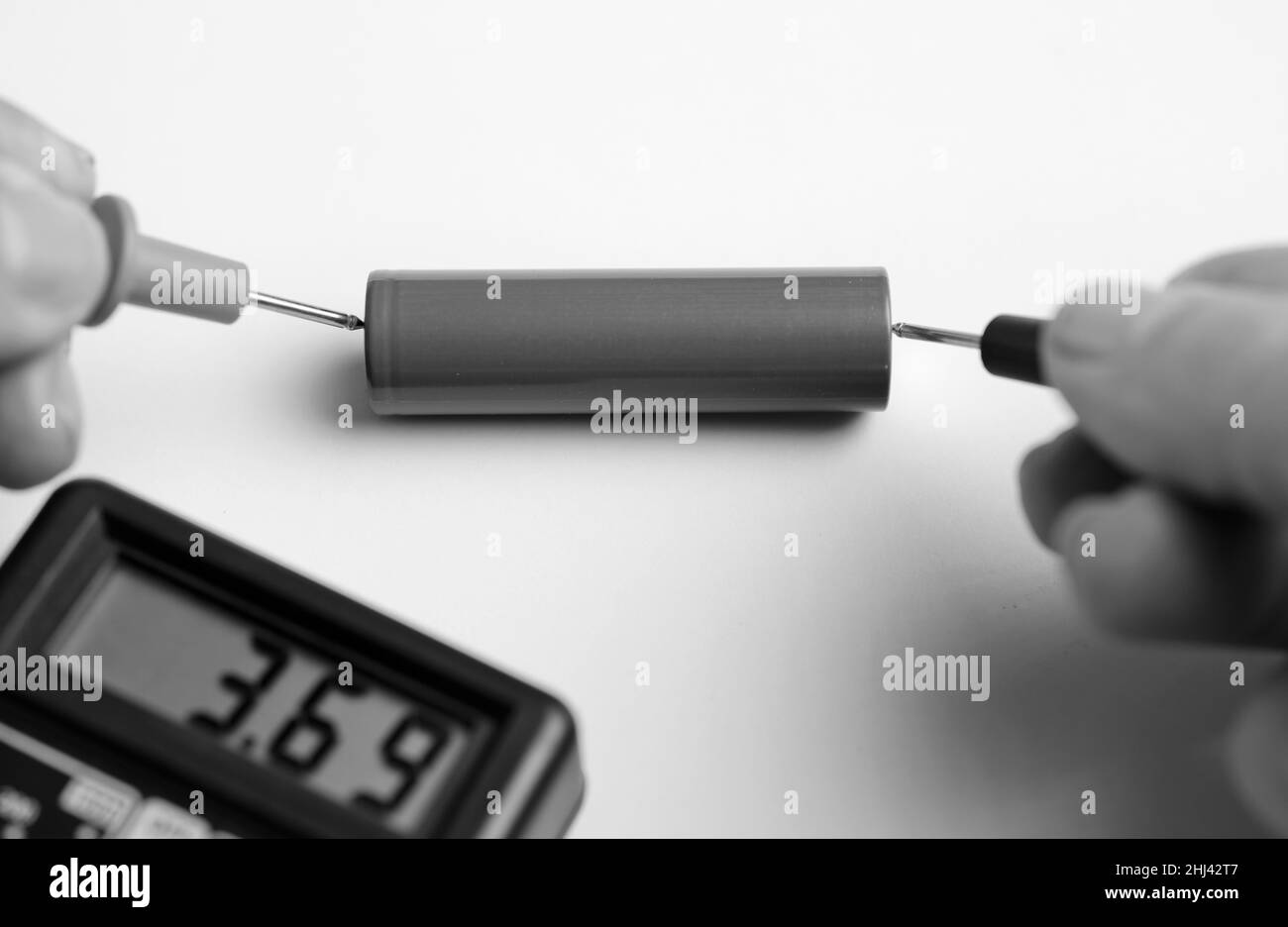 battery with multimeter volt calculator, voltmeter in the hands of a man, red positive pole, black negative pole, on a work table Stock Photo