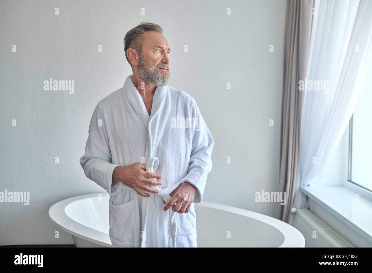 Tranquil pensive adult male belting his towelling robe in the bathroom Stock Photo