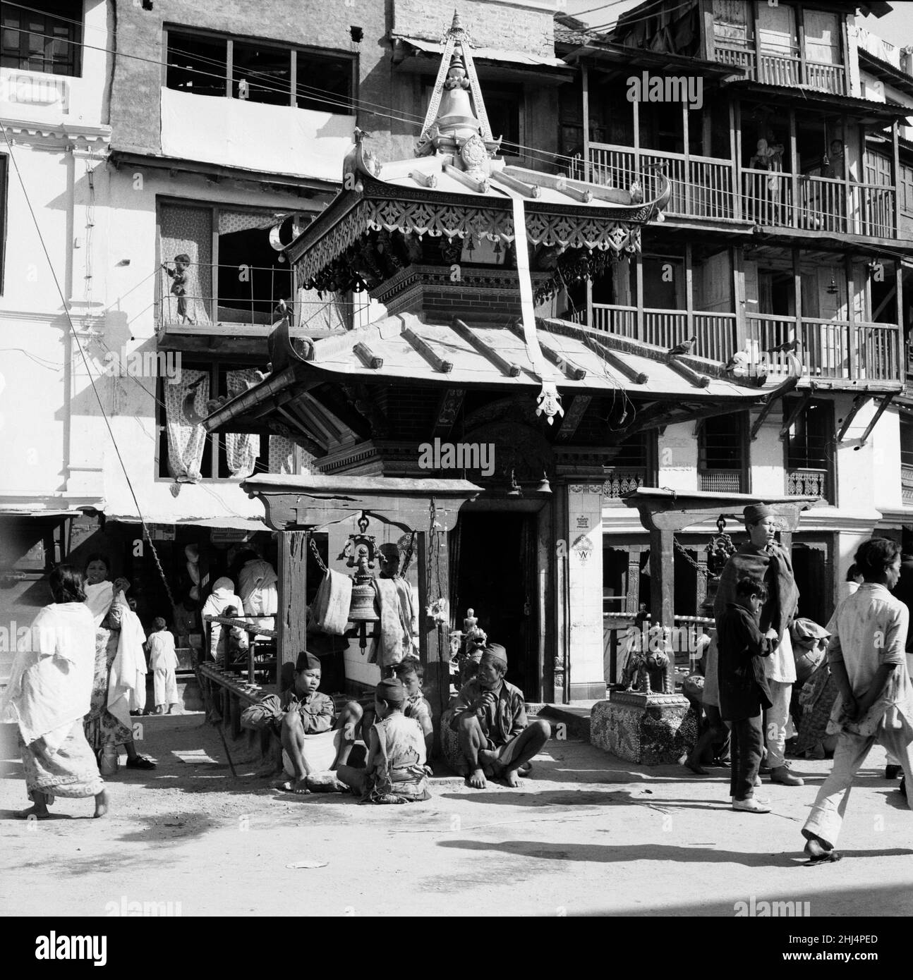 Shoppers pass a shrine to Buddah in one of the main roads leading off Durbar Square in Katmandu, Nepal. February 1961 l l Stock Photo