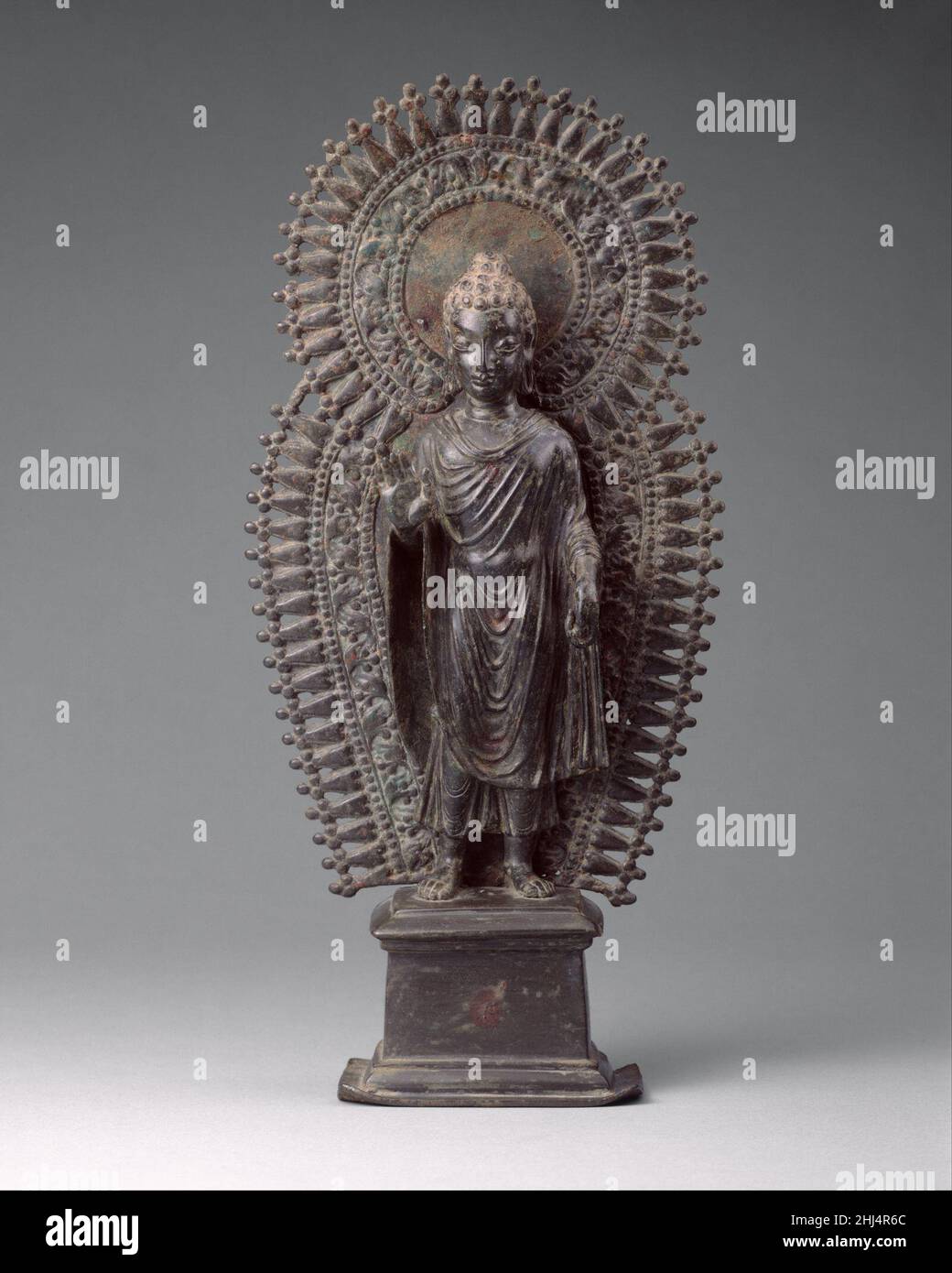 Standing Buddha with Radiate Combined Halo ca. late 6th century Pakistan (ancient region of Gandhara) A few small personal images from Gandhara representing the Buddha have survived. This metal image blends elements seen in the stone sculpture of Gandhara with the Gupta style of north India. Its portability made it an important vehicle for disseminating the Gandharan style to other parts of Asia.. Standing Buddha with Radiate Combined Halo  39165 Stock Photo