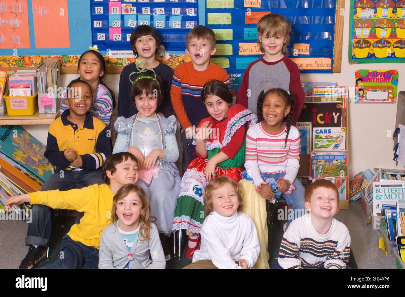 Group of Kindergarten students posing in classroom, two girls wearing dressup clothes Stock Photo