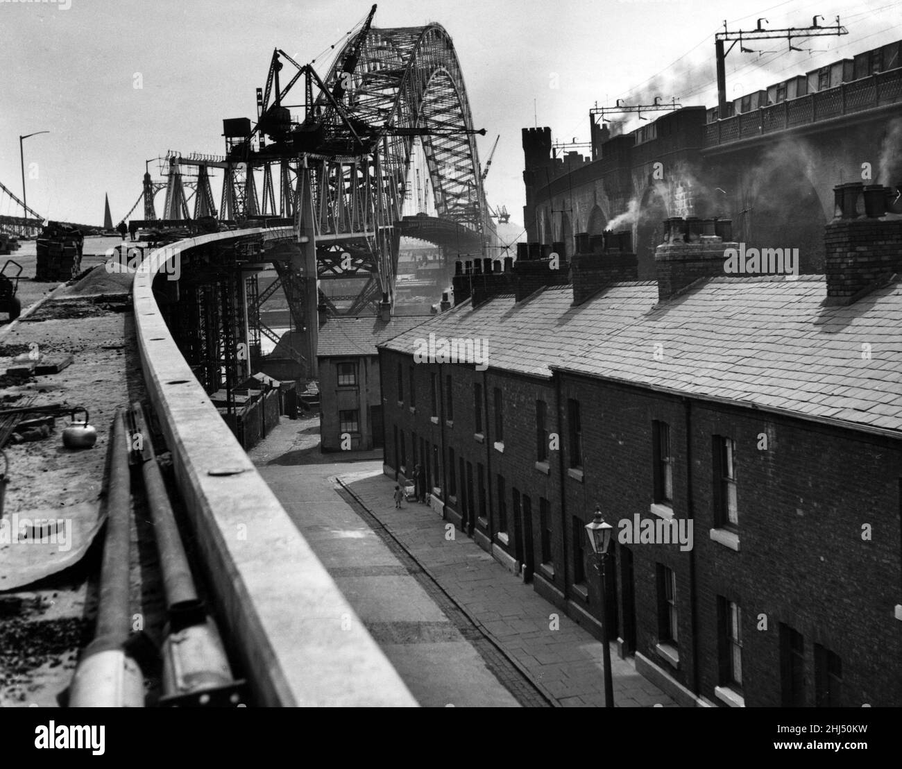 An unusual view of the Widnes-Runcorn Bridge, now almost completed, showing how the approach road soars above the rows of terraced houses in Widnes. On the right is the rail way crossing. 8th June 1961. Stock Photo