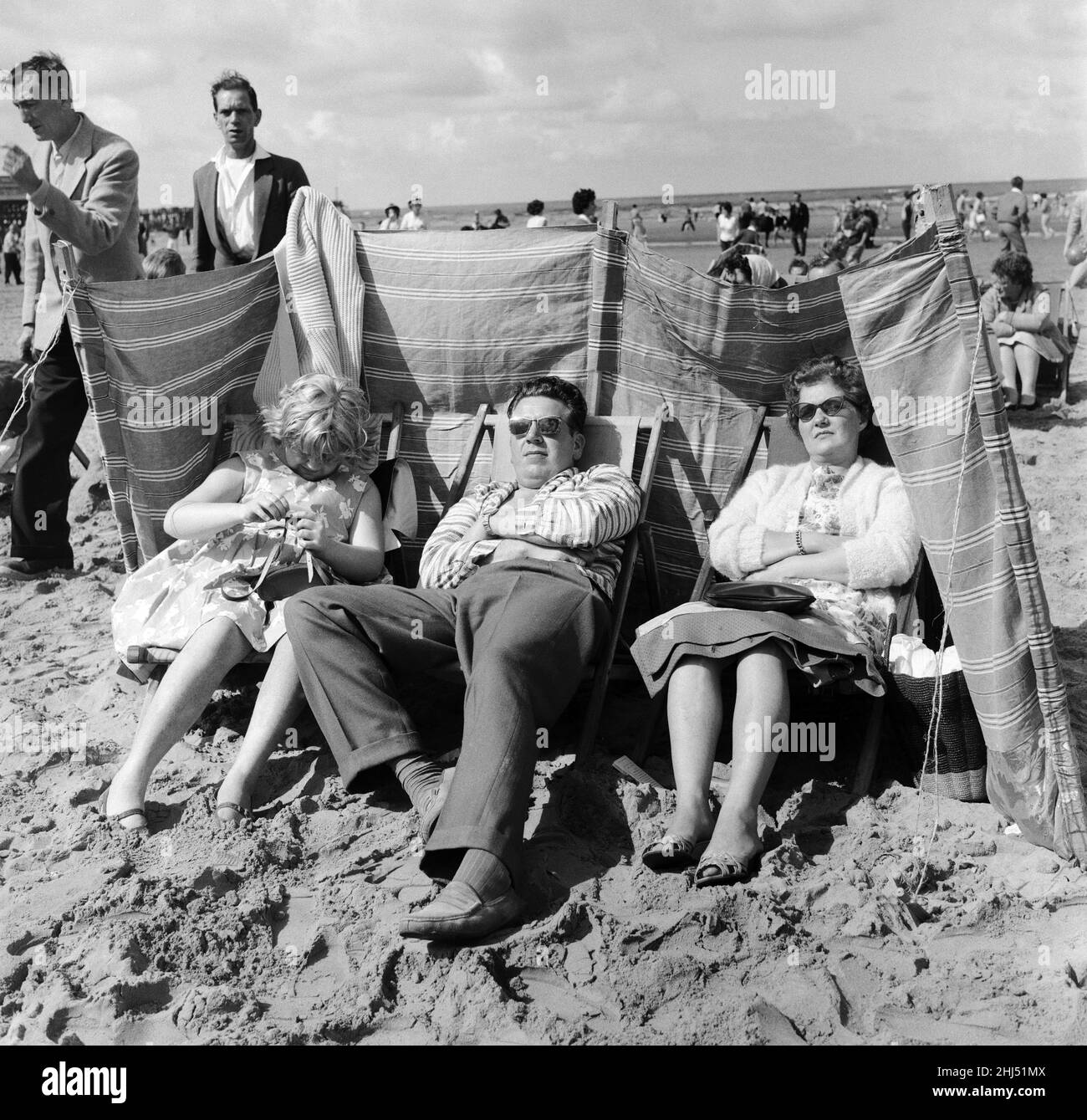 The Lemm family of Castleford, Yorkshire sit behind the protection of their windbreaker during a windy at Blackpool beach in the summer holidays. 6th August 1961. Stock Photo