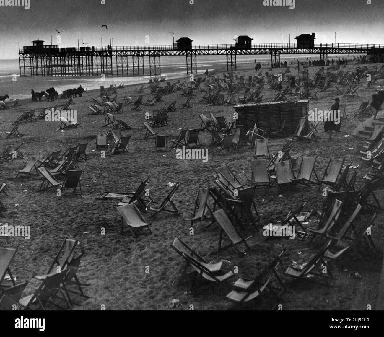 Empty deck chairs sprawl forlornly on the deserted beach at Rhyl after the storm had driven home the holidaymakers. 26th May 1955 Stock Photo