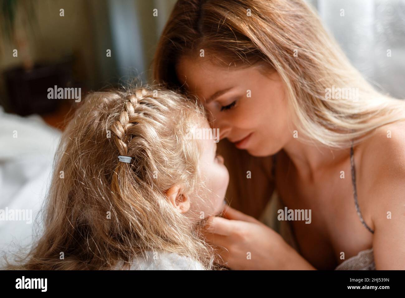 Portrait of blondes mother 30s and daughter 5 years. Beautiful mom gently touches child girl face at home. Loving caring mom show tenderness love to Stock Photo