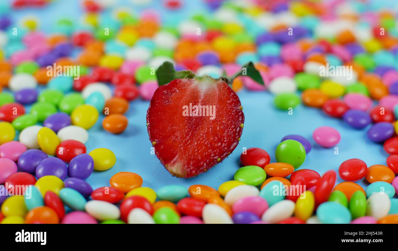 Strawberry among colorful sweet candy on blue pastel background. Stock Photo