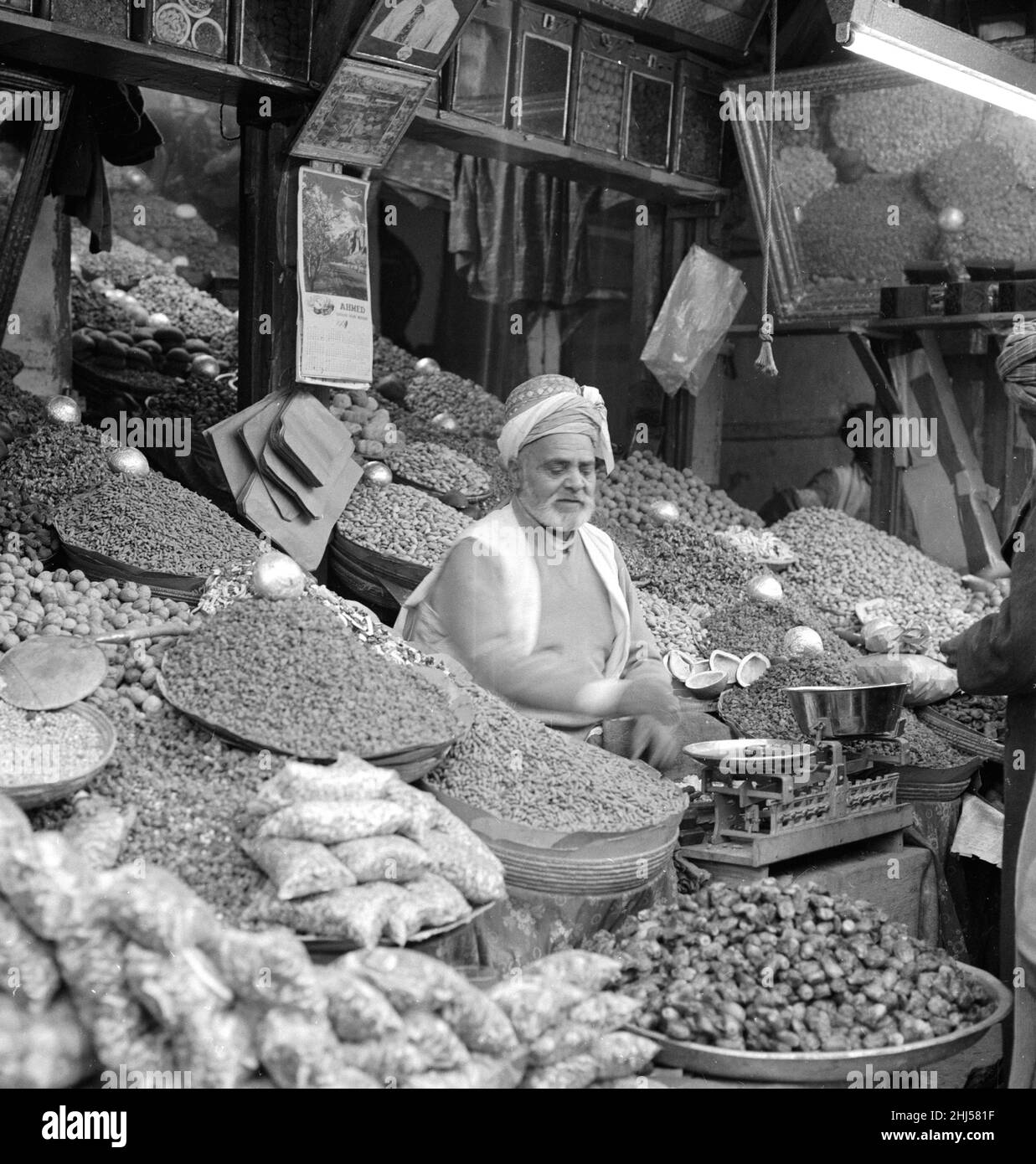 Trader in vegetables and spices sits outside his shop in Peshawar the capital of the North West Frontier province of Pakistan. February 1961  l Stock Photo