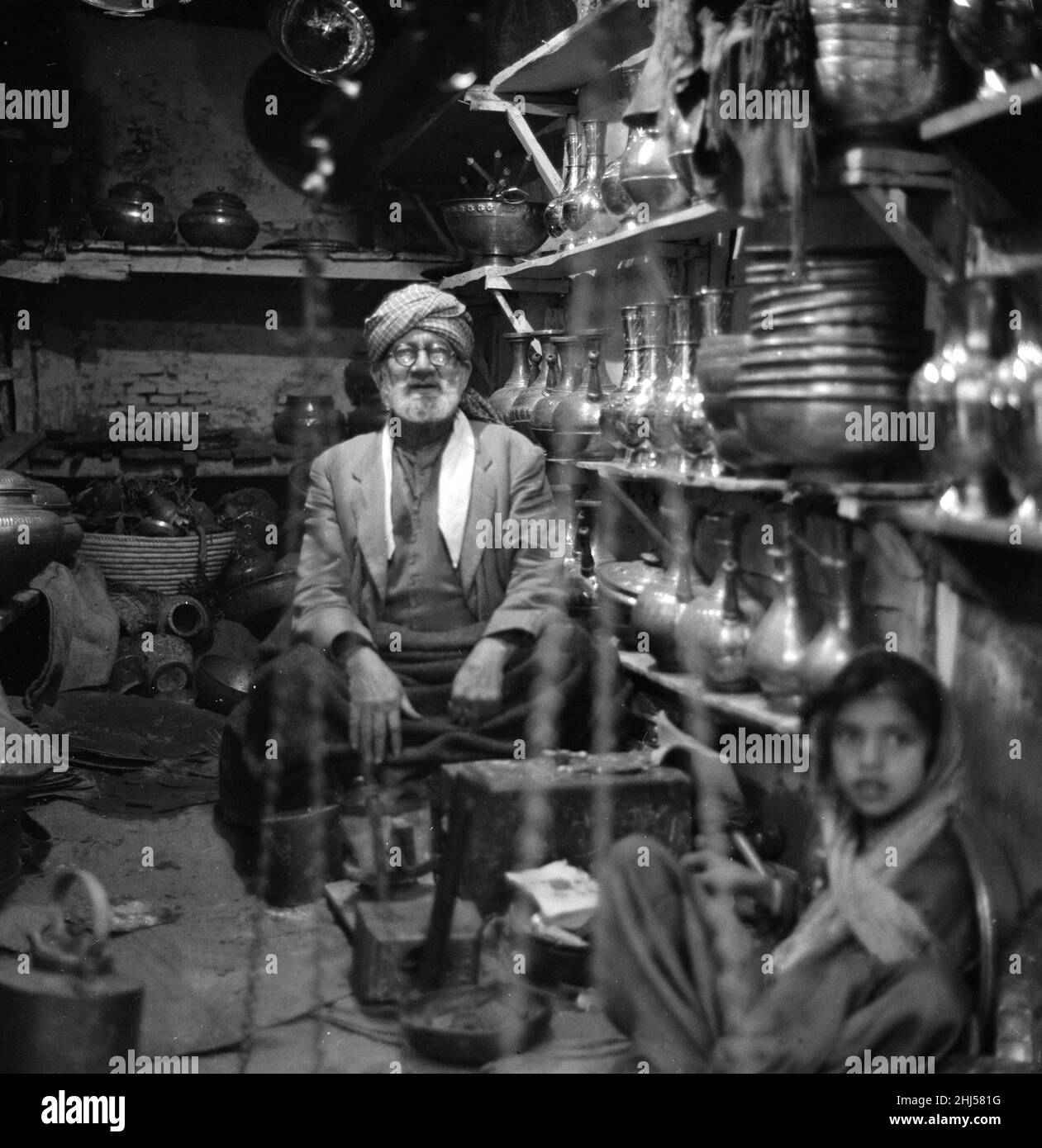 Traders sit inside their shop in Peshawar amongst the pots and pans. Pesthe capital of the North West Frontier province of Pakistan. February 1961  l Stock Photo