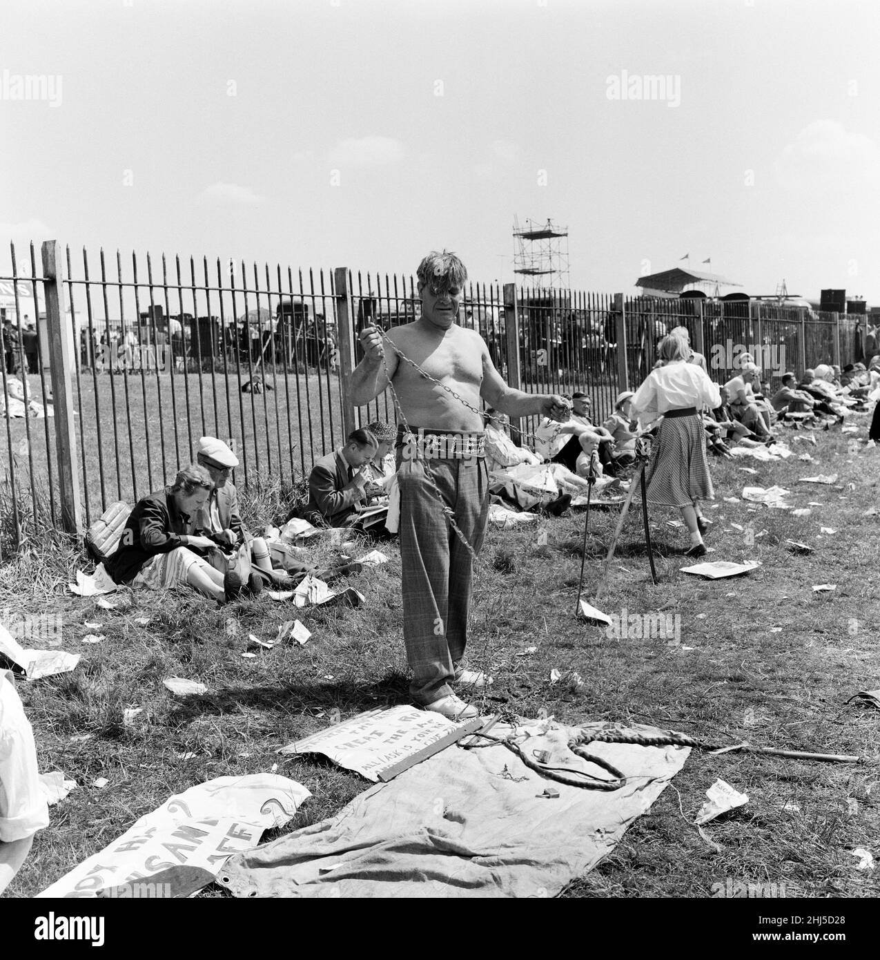 Derby Day at Epsom. Pictured, a strong man prepares to wrap himself in chains, but people in the background are too hot to care. 3rd June 1959. Stock Photo