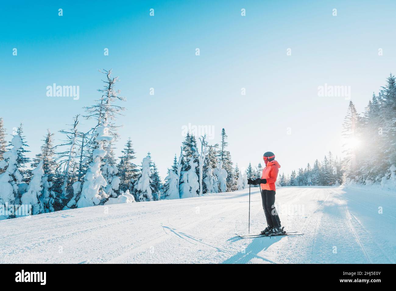 Skiing. Ski portrait of woman alpine skier holdings skis wearing helmet, cool ski goggles and hardshell winter jacket and ski gloves on cold day in Stock Photo