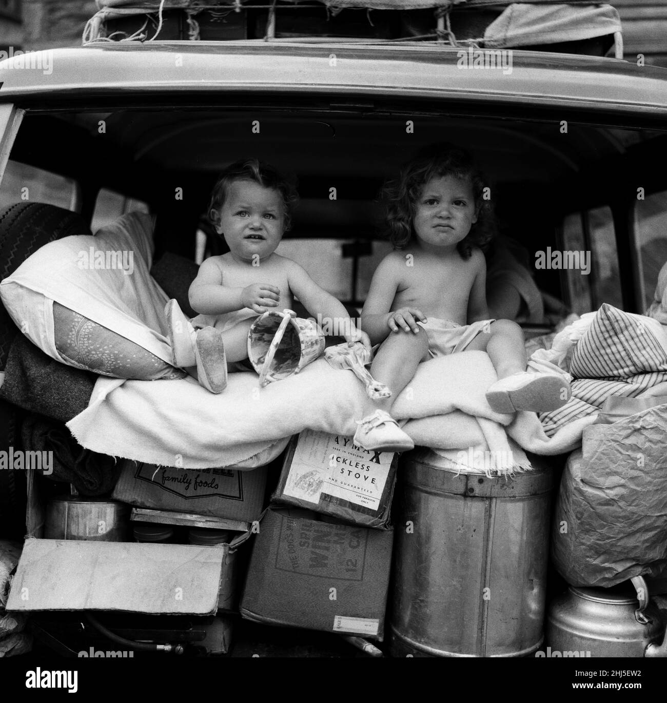 Two seasoned travellers, Paul and Julie Bridgett, aged 11 months and 2 years respectively. On a Cornish touring holiday from St Leonards-on-Sea with mummy, daddy, uncle and auntie in the van which the carrie two tents for sleeping and all the paraphernalia for camping out. The two toddlers keep in a bed at the rear of the van and are so comfortable there that they doze during travel and use it as an observation post when its raining . Mummy is on the seat just behind them to make sure they are safe. The pram is tied on the van roof. They are pictured in their usual position in the van at Looe, Stock Photo