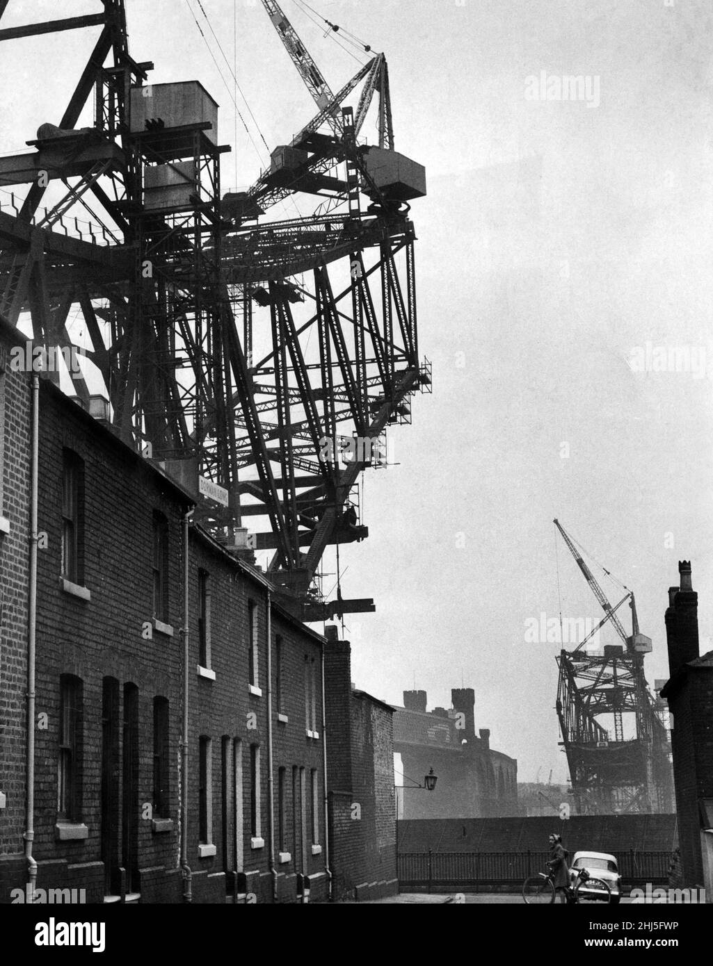 Houses in Runcorn are dwarfed by the new Runcorn-Widnes bridge, which is under construction. 19th March 1960. Stock Photo