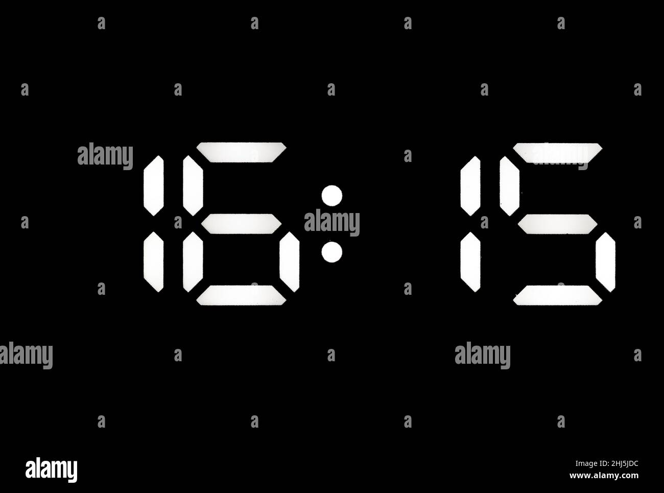 Real white led digital clock on a black background showing time 16:15 Stock Photo