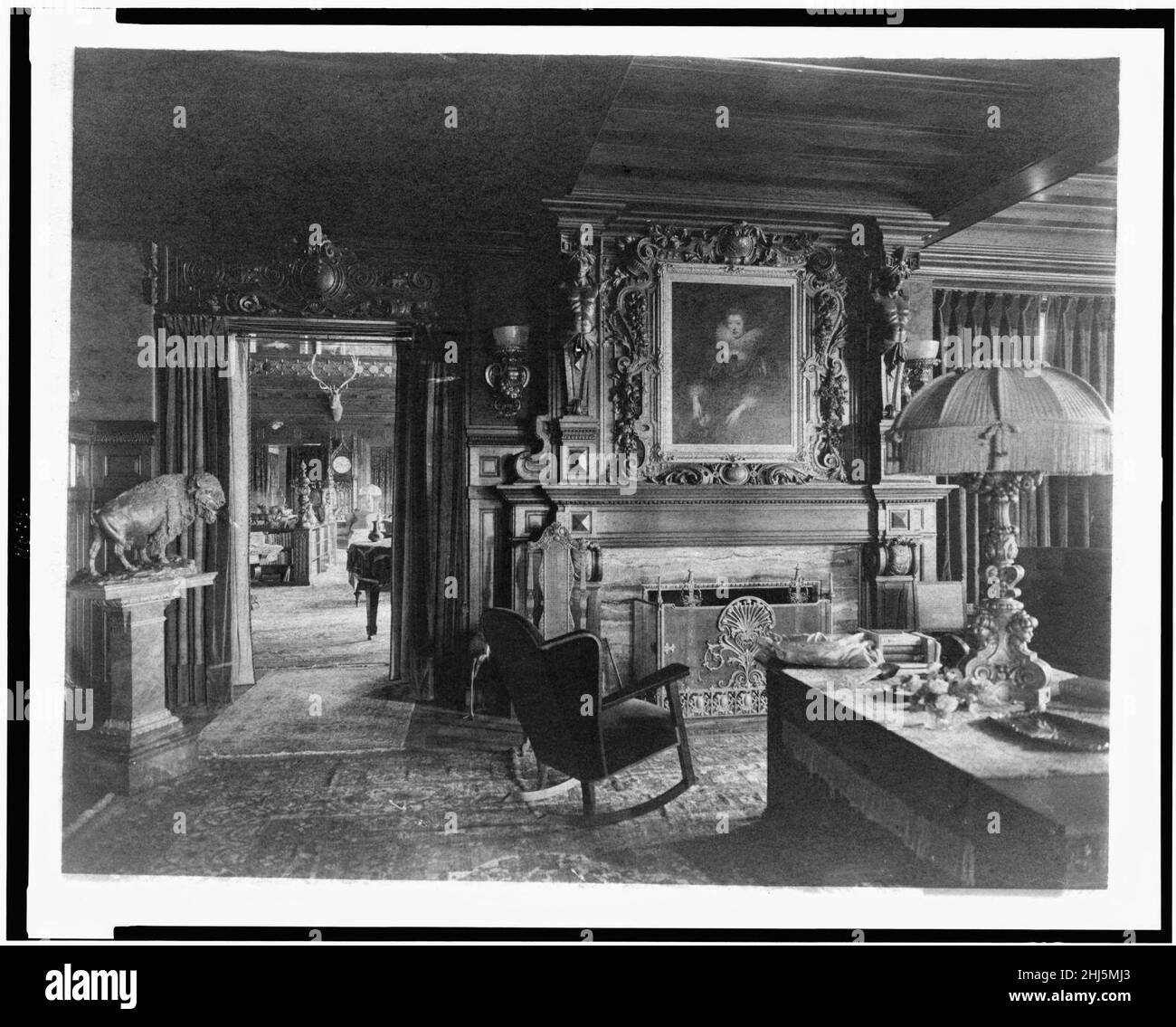 Study with portrait of woman in Elizabethan dress, over fireplace, fringe lamp at right, and buffalo statue on left; elk head on wall and grandfather clock in background, in home of Edmund Stock Photo