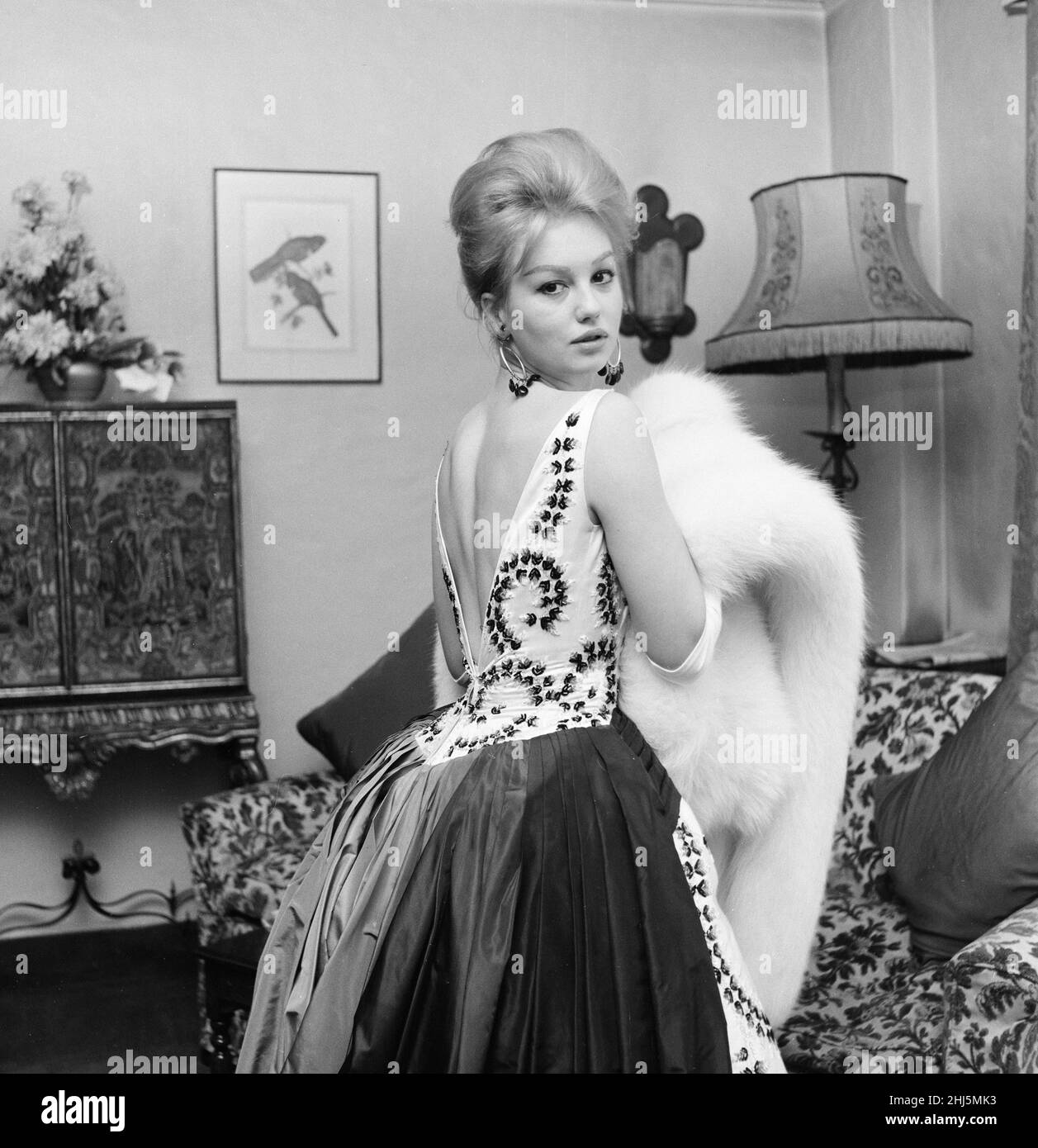 Mylene Demongeot, french actress, gives a preview of the dress she will be wearing at the premier of her new film, The Singer Not the Song, at the Odeon, Leicester Square tomorrow evening, Pictured in her room at The Dorchester Hotel, London, Wednesday 4th January 1961. Mylene Demongeot is wearing a full length full skirt dress of white satin and embroidered with black and white sequins in a leaf pattern, with a big sash of black satin that ties in a bow at the waist, completed with a white fox stole. Stock Photo