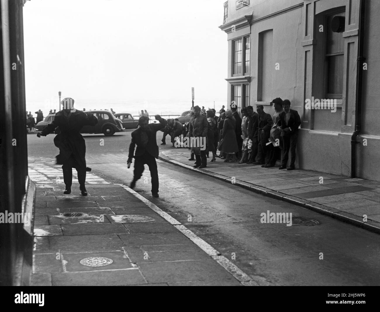 Brighton catches the full force of the gale. Visitors on the seafront find themselves trapped by terrific gusts which make them cling to any support they can find. 29th July 1956. Stock Photo