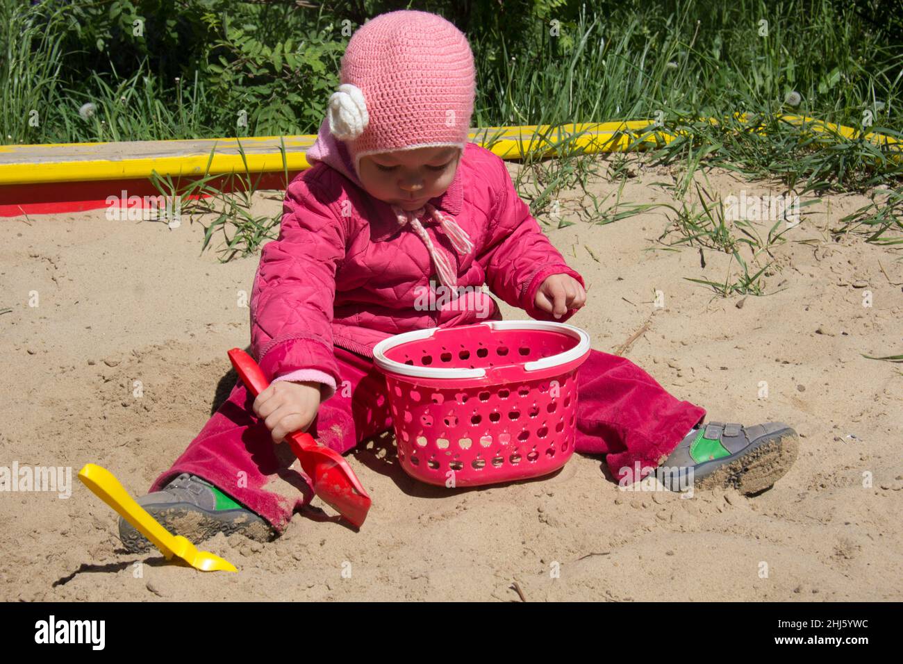 Child of two years old playing with sand and shovel in sandbox on