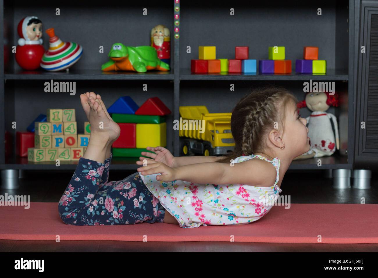 Little girl going to do bow yoga pose as lie on tummy, bend knees, reach arms back towards and