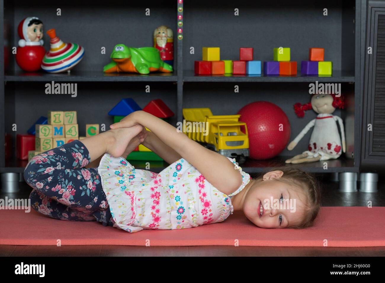 Little girl going to do bow yoga pose as lie on tummy, bend knees, reach arms back towards and