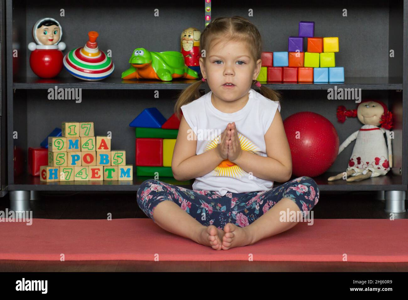 Little girl making yoga pose of cobbler or butterfly as sit on buttocks with tall spine, bend legs, place soles of feet together, and gently flap legs Stock Photo