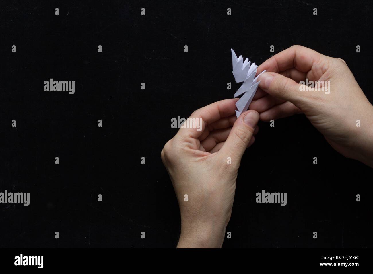 Making snowflake. Step . Woman hands unfolding paper to reveal snowflake on black background Stock Photo