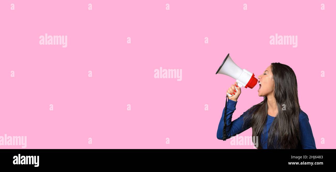 Young woman yelling over a loud hailer or megaphone in a conceptual image on pink with copyspace Stock Photo