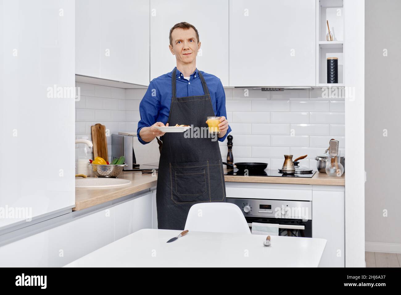 Middle age man brings plate with healthy food to the kitchen table Stock Photo
