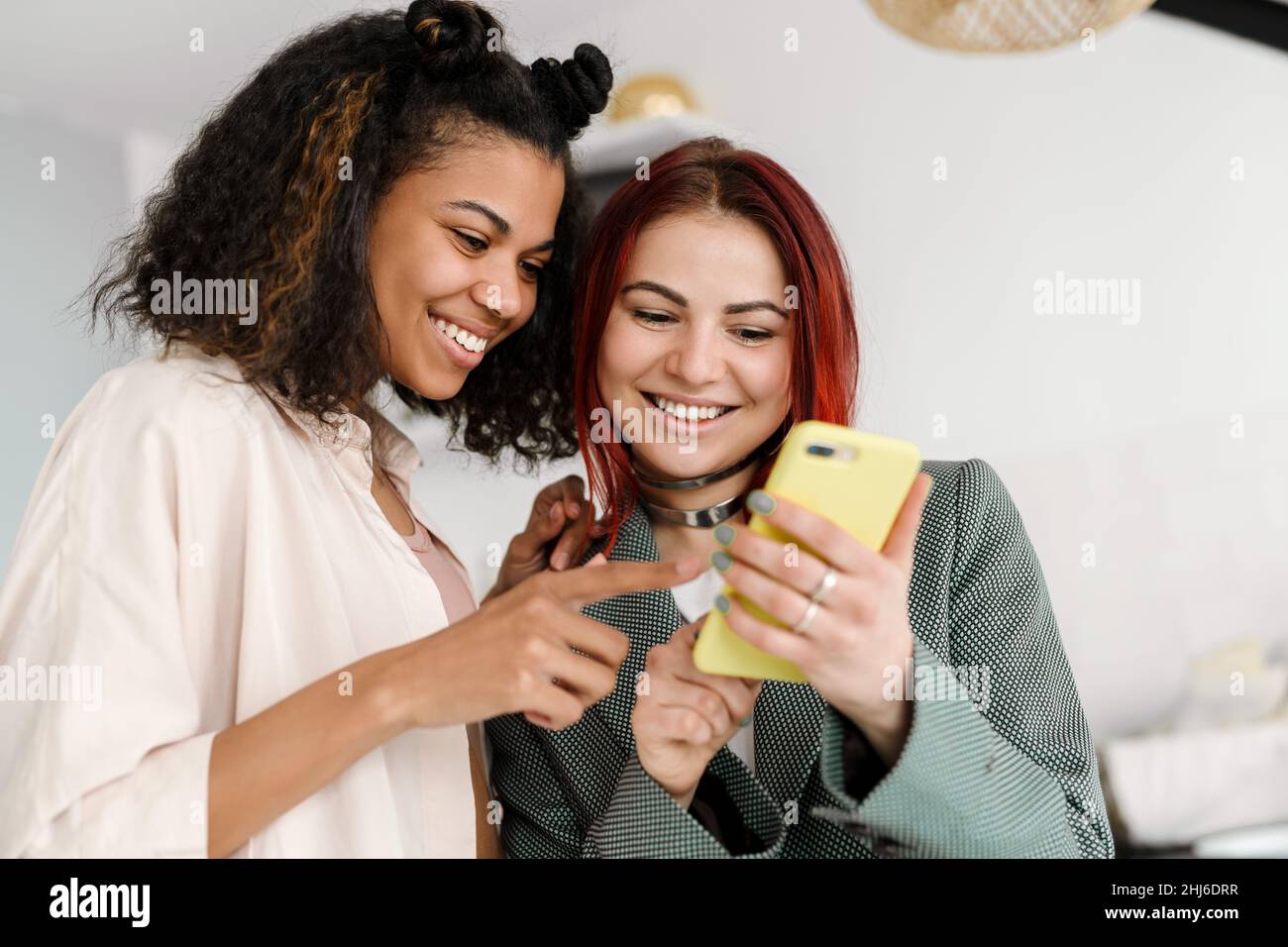 Young multiracial two women smiling while using mobile phone at home Stock Photo