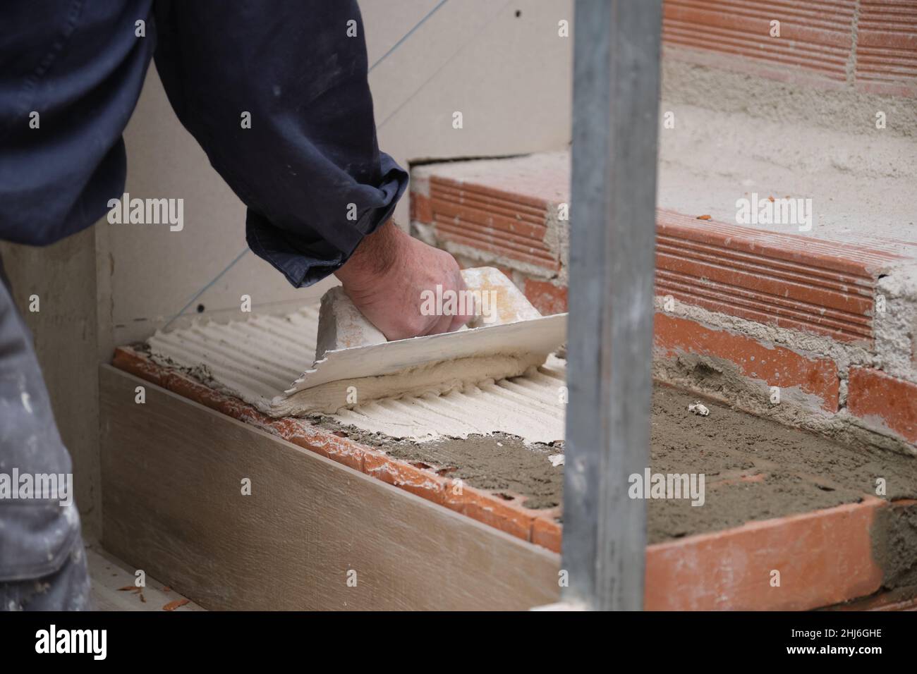 Unrecognizable bricklayer using a notched trowel to build a staircase in a home. Stock Photo