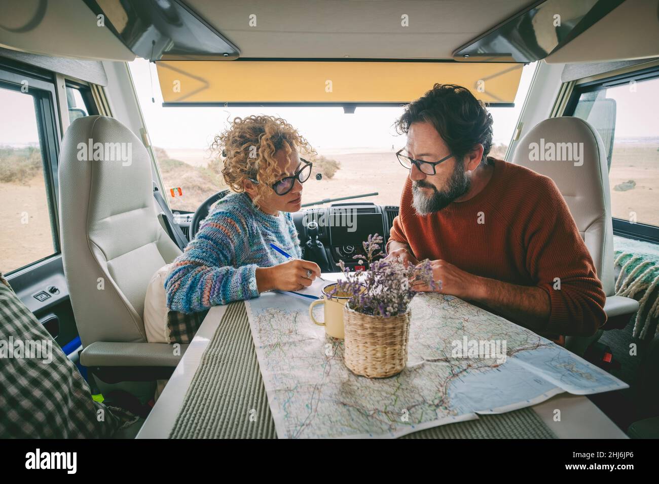 Adult couple planning next travel destination sitting inside a camper van using a paper map guide on the table. ature traveler and vanlife alternative Stock Photo