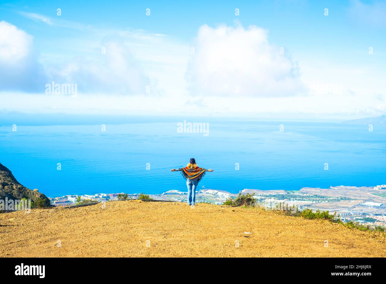 Tourist and freedom lifestyle people travel concept. Woman viewed from back opening arms to enjoy an amazing view and landscape. Blue ocean and sky fr Stock Photo