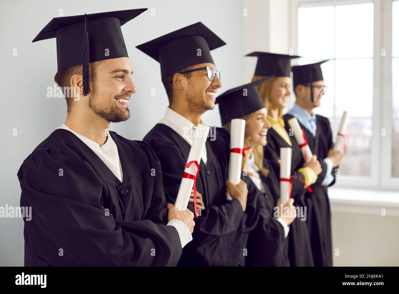 Smiling graduates in row pose with diplomas Stock Photo